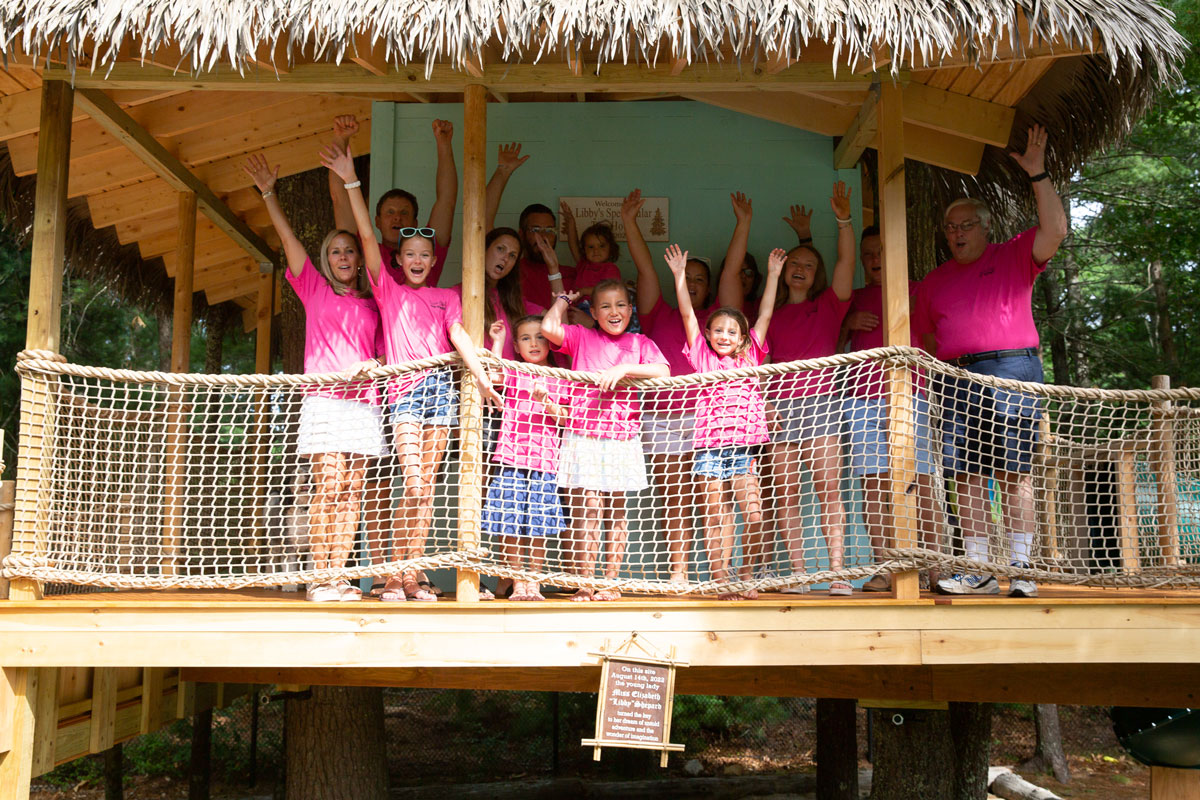 A group of children and adults cheering with raised arms in a wooden treehouse, built for a young girl with leukemia through United Civil's partnership with Make-A-Wish Massachusetts and Rhode Island.