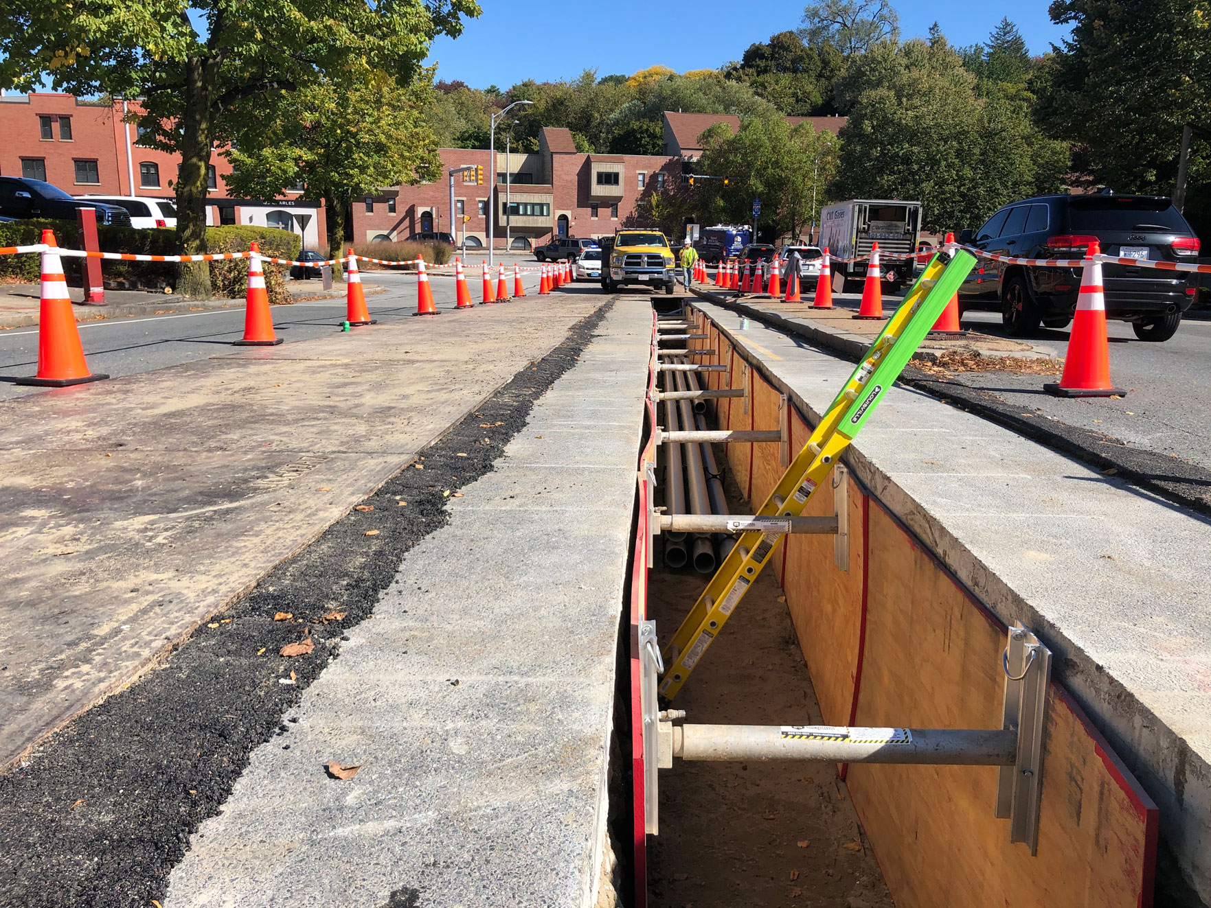 United Civil crew managing an open distribution ductbank trench along a congested urban street with traffic cones and safety barriers