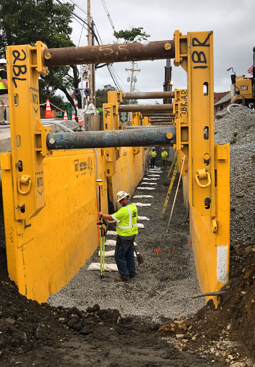 United Civil worker inspecting a deep trench excavation supported by yellow steel trench boxes during underground utility installation
